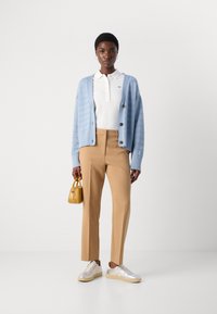 Light blue knitted cardigan with button closure, white polo shirt, tan trousers, silver sneakers, and a small yellow handbag.