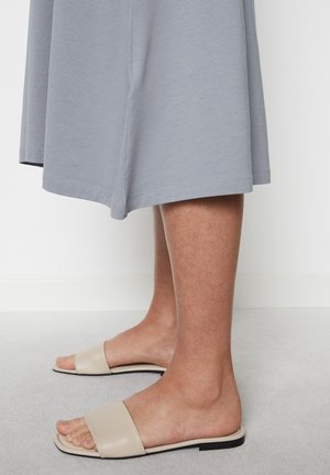 Lichtgrijze jurk tot de knie met een zachte textuur. Beige slide sandalen met een brede band en een platte zwarte zool. Minimalistisch ontwerp.
