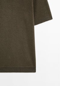 Mørkeolivengrøn kortærmet sweater med et struktureret strikkemønster. Ribstrikkede manchetter og kant, med en afslappet pasform og løs silhuet.
