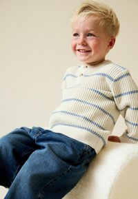 Maglione a righe crema e blu in maglia con scollo rotondo e due bottoni, abbinato a jeans in denim blu. Tessuto morbido, vestibilità rilassata.