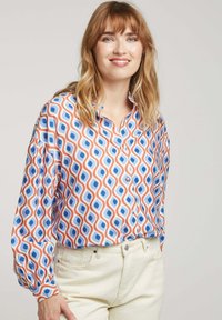 Blouse à manches courtes avec un motif géométrique multicolore en tissu orange, bleu et blanc, avec un devant boutonné et un col à bandes.