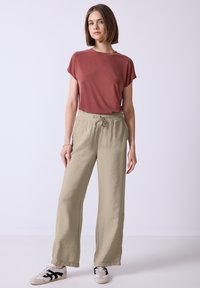 Roestkleurig shirt met korte mouwen en khaki brede broek met een elastische tailleband en koord. Sneakers met zwarte accenten. Gladde textuur.