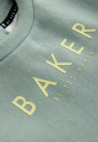 Jasnoniebieski bawełniany sweatshirt z dużym żółtym napisem "BAKER" oraz mniejszym napisem "by TED BAKER". Miękka faktura, krój z okrągłym dekoltem.