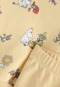 Βαμβακερό ύφασμα σε ανοιχτό κίτρινο χρώμα με διάφορους χαρακτήρες Moomin, εικονογραφημένους σε σκούρο μπλε, με ένα σχεδιαστικό μοτίβο που περιλαμβάνει δέντρα και ήλιο.