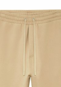 Pantalons de survêtement beige avec taille élastique et cordons de serrage crème, présentant un détail de couture visible au centre avant.