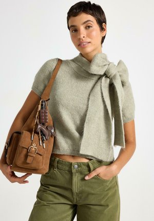 Ljusgrön, kortärmad tröja med en rosettdetalj vid halsringningen. Kombinerad med olivgröna byxor och en brun mockaväska med metalldetaljer.