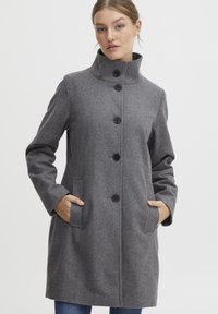 Manteau en laine grise avec col haut, fermeture à boutons sur le devant, deux poches latérales et manches longues. Texture lisse et silhouette ajustée.