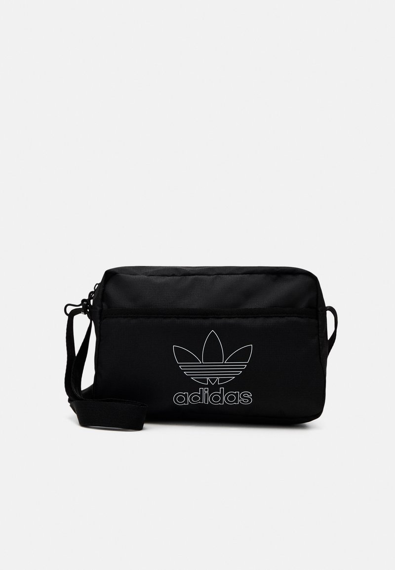 Sac à bandoulière noir Adidas en tissu ; il dispose d'une fermeture éclair, d'une sangle réglable et d'un motif de logo blanc sur le devant.