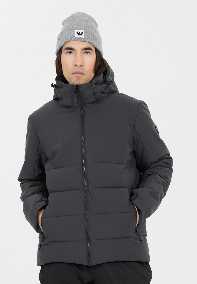 Schwarze Pufferjacke mit Reißverschluss, gepolstertem Design, hohem Kragen und verstellbarem Kapuze; getragen über einer grauen Mütze mit Logo-Patch.