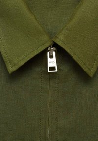 Olive green shirt featuring a structured collar and a central zipper. The fabric has a fine texture with a smooth finish. Zipper pull marked "MNG."