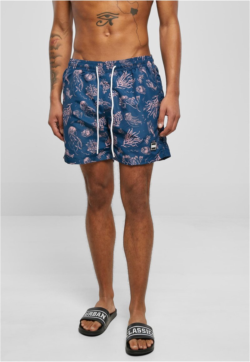 Bañador de color azul marino con un patrón de medusas rosas y coral, cinturilla elástica con cordón blanco y parche de logo en el dobladillo.