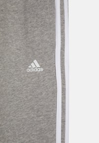 Szare dresy wykonane z mieszanki bawełny, z białymi paskami po bokach i białym logo Adidas z przodu. Miękka faktura i swobodny design.