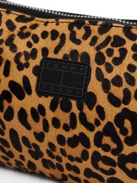Pochette en faux fourrure léopard marron et noir avec un patch logo rectangulaire noir. Elle dispose d'une fermeture éclair et d'une texture douce.