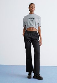 Sweatshirt cinza cortado com o logo "NIKE 1972", combinado com calças largas pretas e botas pretas robustas, com um fundo liso.