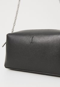 Black leather bag with a textured finish, featuring a silver chain strap and a subtle embossed letter "I" on the front.