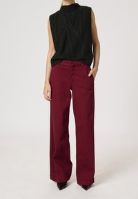 Top negro sin mangas con diseño de punto de cable, combinado con pantalones burdeos de talle alto y pierna ancha; unos tacones negros brillantes completan el look.