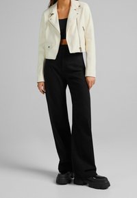 Kremowa skórzana krótka kurtka motocyklowa z zamkiem błyskawicznym z przodu i kieszenią, zestawiona z czarnymi szerokimi spodniami z wysokim stanem i masywnymi czarnymi butami.