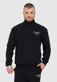 Pullover in pile nero con colletto alto e zip a un quarto. Presenta un logo bianco del marchio e un tessuto morbido e texturizzato.