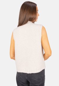 Ärmellose cremefarbene Weste aus strukturiertem, flauschigem Stoff mit unregelmäßigem Saum. Einfaches Design, keine sichtbaren Beschläge oder Muster.