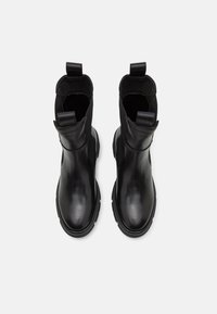 Černé kotníkové boty vyrobené z hladké kůže, s elastickými bočními panely, kulatou špičkou a silnými gumovými podrážkami. Obsahují poutka pro snadné obouvání.