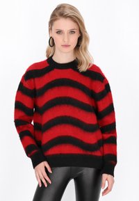Maglione a righe rosse e nere con una texture morbida, collo a giro e maniche larghe. Abbinato a pantaloni neri aderenti.