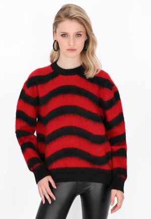 Maglione a righe rosse e nere con una texture morbida, collo a giro e maniche larghe. Abbinato a pantaloni neri aderenti.