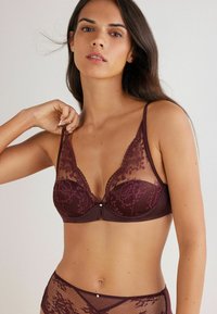 Soutien-gorge en dentelle bordeaux avec des panneaux en résille transparente, motifs floraux, décolleté plongeant, bretelles ajustables et un accent décoratif en perle au centre.
