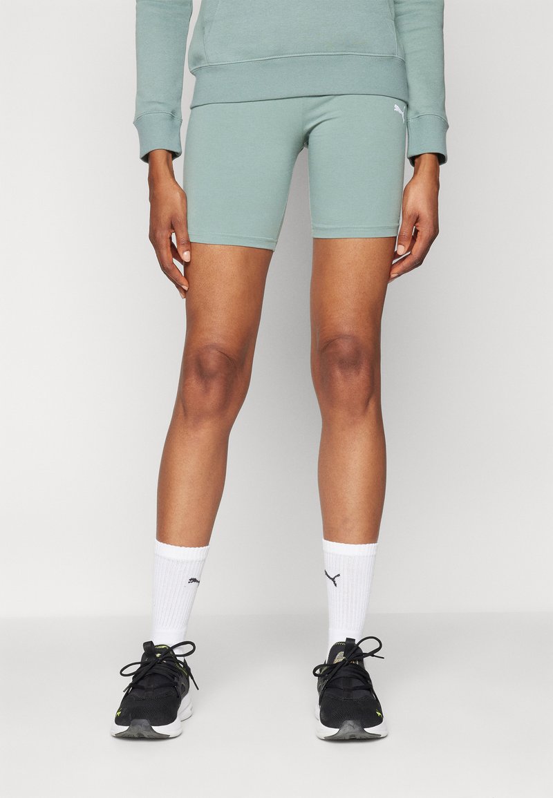 Pantalones cortos deportivos de color verde claro y un sudadera a juego, con una textura suave. Se llevan con zapatillas negras y calcetines blancos con un logo.