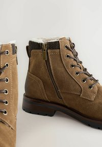 Ruske putne čizmice od suede materijala s patentnim zatvaračem i vezanjem, sa mekanim bijelim podstavom i čvrstom crnom petom.