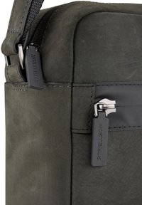 Graue Leder-Messenger-Tasche mit glatter Textur, schlankem Design, einem Reißverschluss mit silberner Hardware und einem markierten Reißverschlussanhänger.