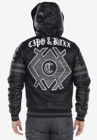 Black hooded jacket with textured leather panels, featuring white branding and geometric designs on the back. Includes striped accents on sleeves.