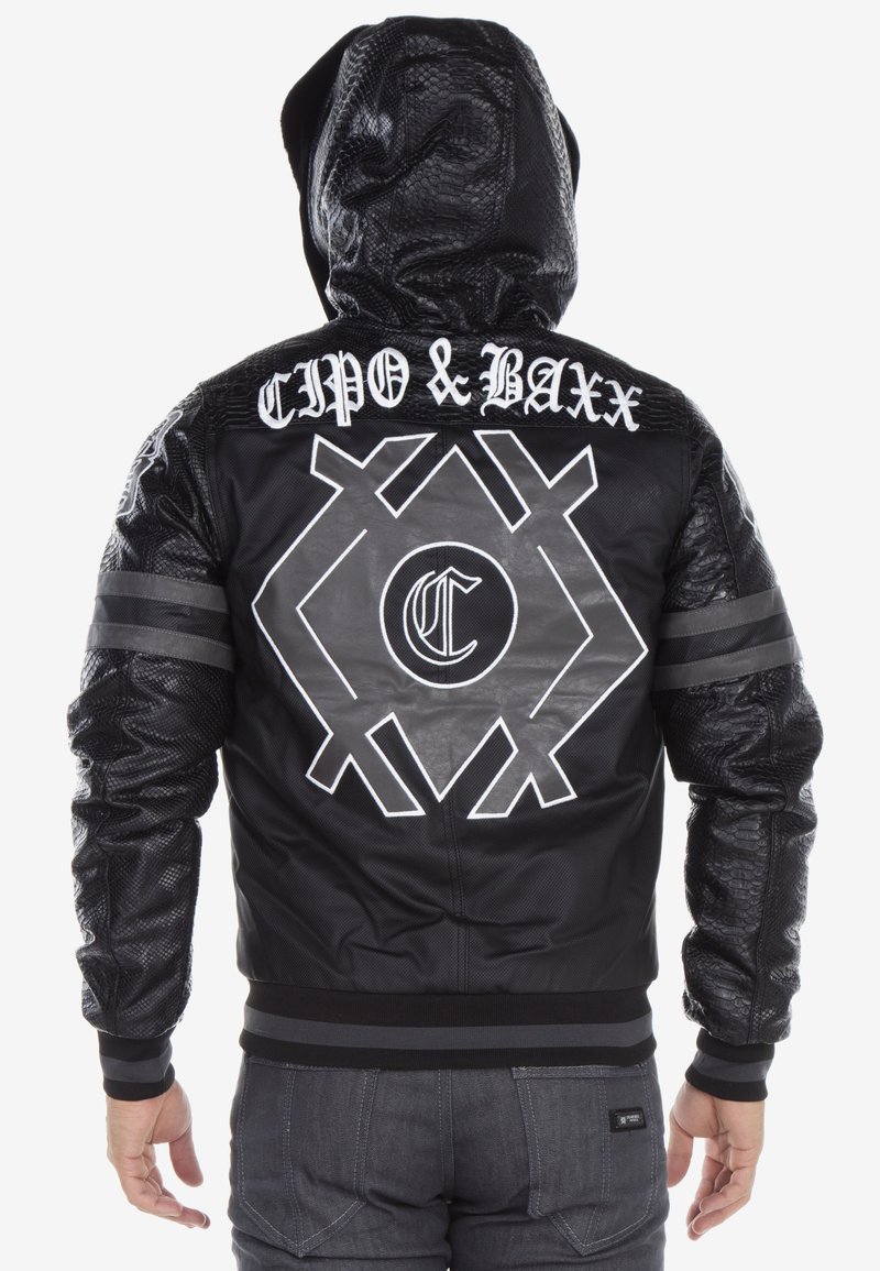 Schwarze Bomberjacke aus Kunstleder mit strukturierter Kapuze, weißem Logo und geometrischen Mustern auf dem Rücken sowie gestreiften Akzenten an den Ärmeln.