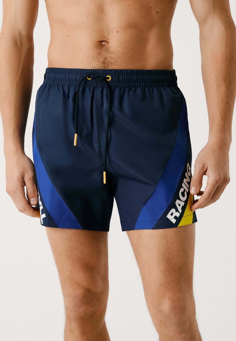 Mornarske kopalne hlače z modrimi stranskimi paneli, rumenimi poudarki, elastičnim pasom s vrvico in natisnjenim napisom "RACING."