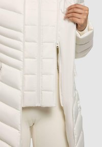 Witte gewatteerde jas met verticale stiknaden, dubbele ritsen en ribbeltextuur. Heeft een slim-fit ontwerp met een gladde, glanzende afwerking.
