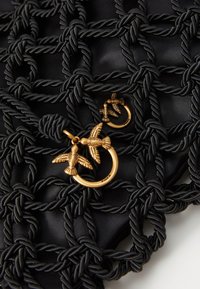 Zwarte geweven tas met een gevlochten touwontwerp, benadrukt door gouden hardware accenten in de vorm van vogels. Zachte textuur met ingewikkelde details.
