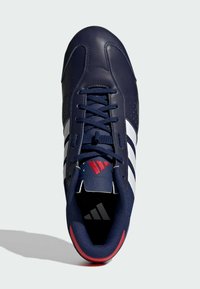 Laivansinis urheilukenkä, jossa on nahka päällinen, valkoiset raidat, punaiset yksityiskohdat ja teksturoitu kieli. Nauhat samassa laivansinisessä värissä.