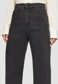 Jean noir en denim avec taille haute, ornés de strass décoratifs, fermeture éclair et poches latérales. Texture lisse et design à jambe droite.