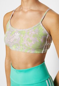 Sutiã desportivo Adidas com estampa de serpente em verde pastel e rosa, tecido leve, alças largas e pequeno logótipo branco na frente.