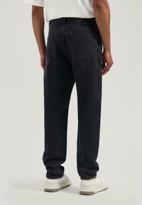 Czarne dżinsy o prostym kroju, z widocznymi tylnymi kieszeniami, minimalnym wykończeniem i wytrzymałą pętlą do paska. Noszone z białymi sneakersami.