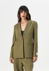 Olive green blazer with notched lapels, single button closure, and front pockets. Structured design and smooth fabric texture.
