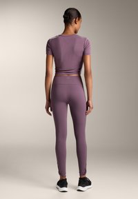 Top scurt, fitted, de culoare purpurie, cu mâneci scurte și colanți cu talie înaltă, amândouă din material elastic. Colanții au fante pe lateral, la gleznă.