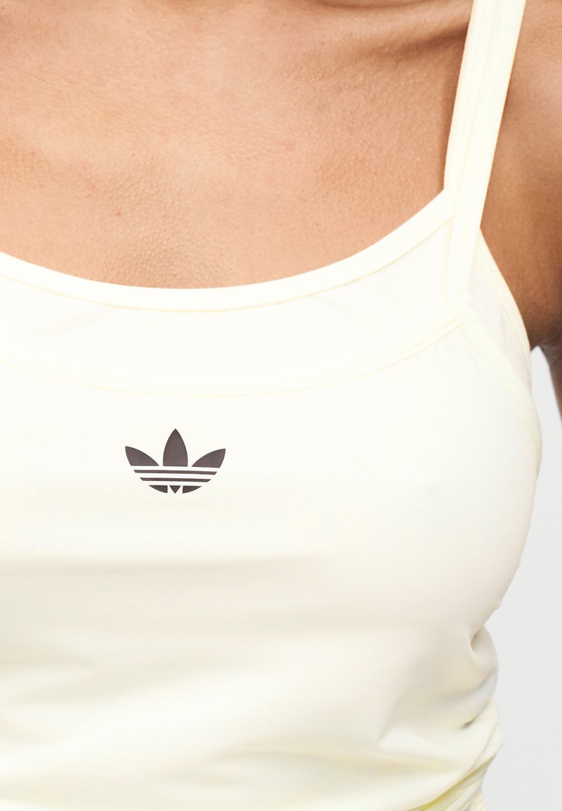 Débardeur de sport jaune clair avec un design à fines bretelles. Présente un logo Adidas noir centré sur la poitrine. Texture lisse.