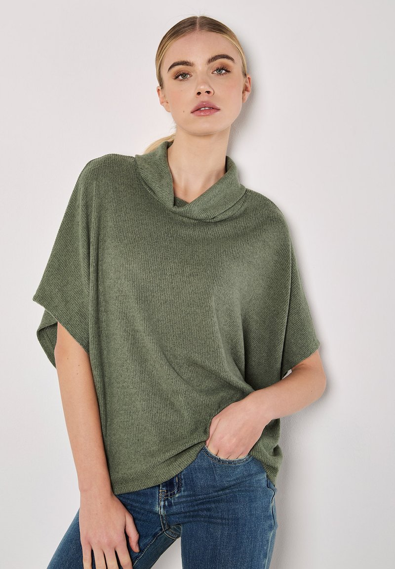 Pull en maille côtelée vert avec un col bénitier, des manches courtes et une coupe ample, associé à un jean bleu ajusté.