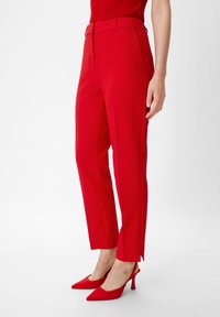 Pantalons tailleur rouges à coupe slim, avec une texture lisse, poches avant et une petite fente à l'ourlet. Accompagnés de talons assortis rouges.
