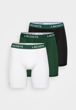 Fehér boxeralsó zöld Lacoste logós derékrésszel, testhezálló kialakítással, sima textúrával és combközép hosszúsággal.