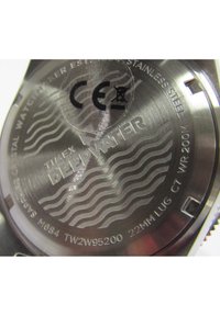 Le fond de boîtier en acier inoxydable de la montre présente une gravure "TIMEX DEEPWATER", un marquage CE, et un design en motif de vagues avec des détails de résistance à l'eau et le numéro de modèle.