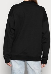 Sweat-shirt noir avec un col rond et des épaules tombantes. Fabriqué en tissu doux, il présente des poignets et un ourlet côtelés, avec une coupe décontractée.