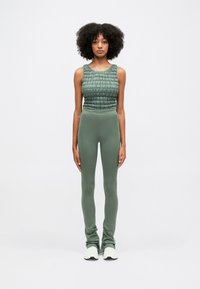 Πράσινο κοντό τανκ κορμάκι με υφή, συνδυασμένο με εφαρμοστά πράσινα κολάν. Το σύνολο διαθέτει αόρατη ζώνη και μαλακό ύφασμα.