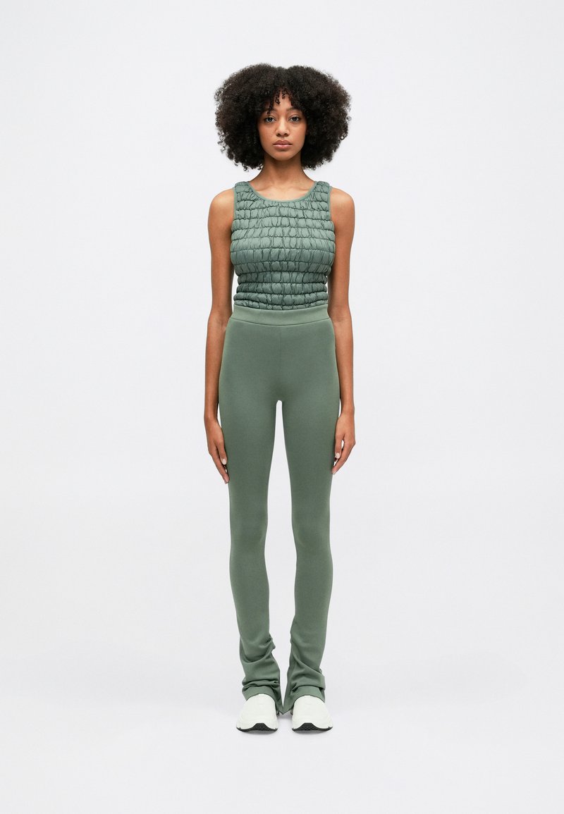 Πράσινο κοντό τανκ κορμάκι με υφή, συνδυασμένο με εφαρμοστά πράσινα κολάν. Το σύνολο διαθέτει αόρατη ζώνη και μαλακό ύφασμα.