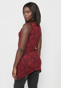 Top sans manches à motif floral rouge avec un ourlet arrondi, fabriqué en tissu léger. Présente un design noir contrastant sur fond rouge.